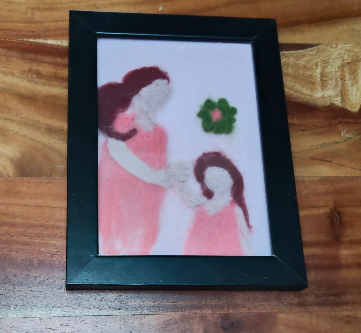 Framed artwork of a woman and child holding hands with flowers, needle felted .